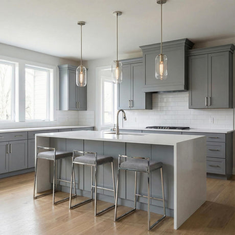 A transitional kitchen with three Liv 11" Clear Capsule Pendants in polished nickel and clear glass hanging over a white waterfall island and gray shaker cabinets.