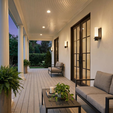 A Colonial porch with Luna LED Outdoor Wall Sconce fixtures in matte black flanking glass doors on white stucco at twilight, featuring gray decking and ferns.