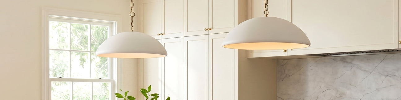 Two Charlie Large Dome Pendants in matte white shown in a bright kitchen with cream cabinetry and carrara marble backsplash.  