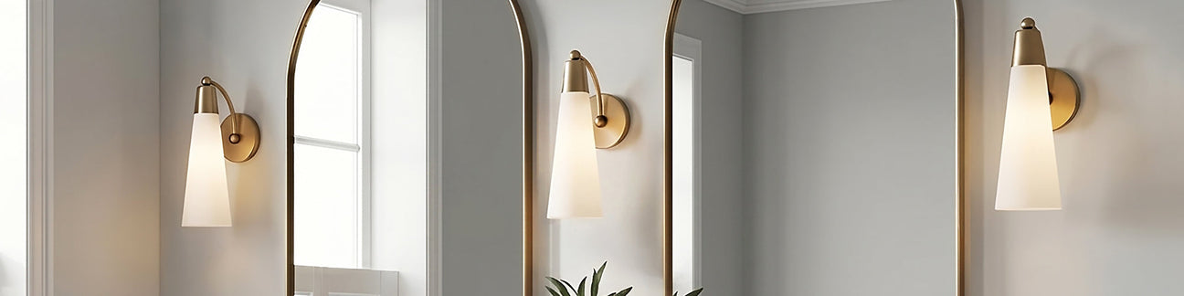 Three Ethel Wall Sconces, Aged Brass and Opal Glass, shown above a double vanity with arched brass mirrors and gray walls.