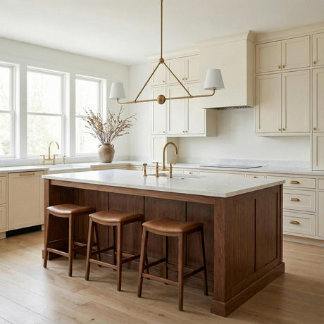 A transitional kitchen features the Banks 2 Shade Linear Pendant 42", White and Brass with brushed accents suspended over a white marble island and cream shaker cabinets.