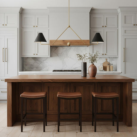 A transitional kitchen features the Banks 2 Shade Linear Pendant 54", Matte Black and Brass hanging over a wood island with three leather barstools and marble backsplash.