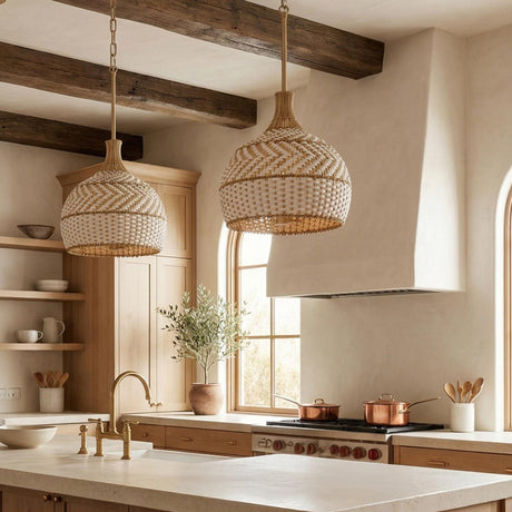 A farmhouse kitchen with two Sienna Medium Pendant 14", Rattan and Soft Brass fixtures hanging over the island, featuring dark wood beams and a plaster range hood.