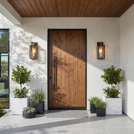 A modern home entry with the Orin Outdoor Wall Light in bronze with vintage brass accents flanking a wood door on white stucco with marble planters.