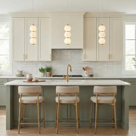 A contemporary kitchen with three Shai LED Pendant 7", Aged Brass and Opal Glass fixtures over the island featuring sage green cabinets and white subway backsplash.