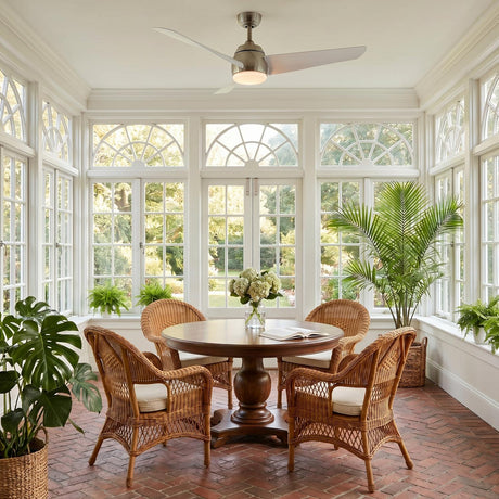 A coastal sunroom with a brushed nickel and white Lorain LED Ceiling Fan featuring a frosted glass light kit above a round table and brick flooring.
