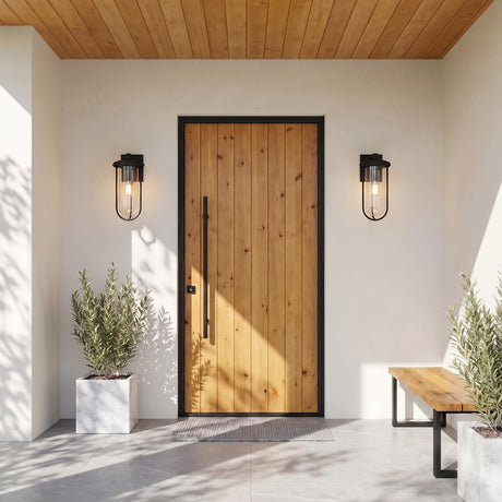 A modern home entry with glowing matte black Orson Outdoor Wall Light, Medium 18" Black fixtures flanking a wood door on white stucco under a wood ceiling.