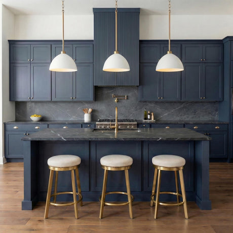 A transitional kitchen features three Cleo Pendant 13", White and Aged Brass fixtures hanging over the island, navy blue cabinetry, and dark marble countertops.