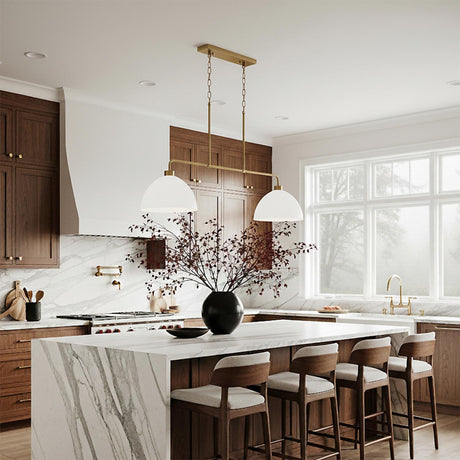 A transitional kitchen with the Cleo 2 Light Linear Pendant 44", White and Aged Brass hanging over the white marble waterfall island and dark wood cabinets.