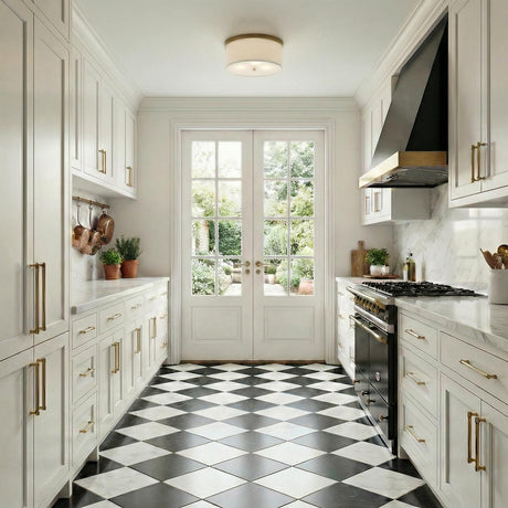 A transitional kitchen features the Wells Flush Mount 16", Aged Brass with a linen drum shade along the ceiling center above white cabinetry and checkered marble floors.