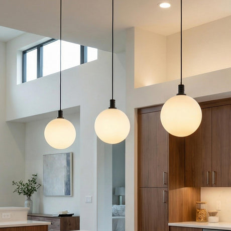 A modern kitchen featuring three Soren LED Pendant 5" matte black and opal glass globe pendants over a white island with wood cabinetry and a double-height ceiling.