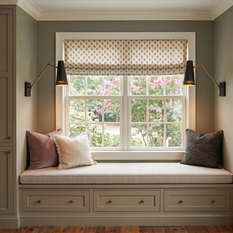 A transitional living room featuring the Darien Articulating Wall Sconce in matte black and brushed brass flanking a window above a sage green built-in window seat.