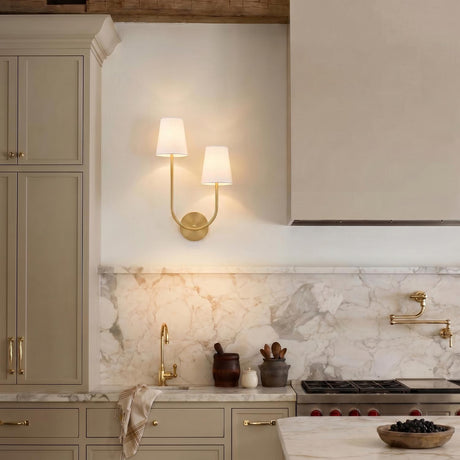 A transitional kitchen featuring a Greta Double Wall Sconce, Satin Brass with linen shades, mounted on a marble backsplash beside taupe cabinets under a beamed ceiling.