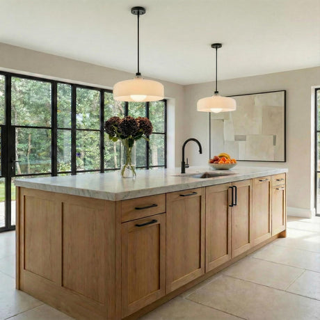 A transitional kitchen features two Alder Pendant 15", Black with Milk Glass pendants in a matte black finish over a marble island with light oak cabinetry.