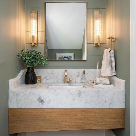 A transitional bathroom with two antique brass Stratton Wall Sconce 20" fixtures flanking a mirror over a white marble vanity and sage green shiplap.