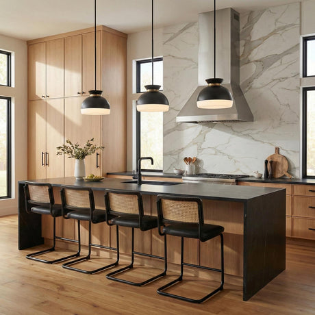 A modern kitchen features three Elody Medium Pendant 15", Matte Black and Brass fixtures over a black waterfall island with cane counter stools and marble backsplash.