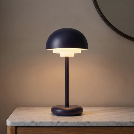 A minimalist entryway featuring the Carola Rechargeable Table Lamp 12", Navy Blue with a tiered shade on a white marble console table beside a dark round mirror.
