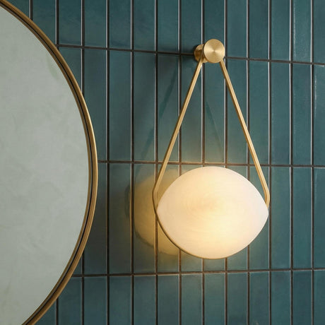 A contemporary bathroom featuring the Maxine LED Wall Sconce in aged brass and matte cloud glass mounted on a teal vertical stacked tile wall beside a mirror.