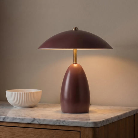 A modern living room with the Aubrey Rechargeable Table Lamp 11", Maroon featuring a brushed brass stem on a white marble topped wood console.