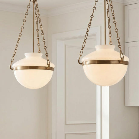 A transitional kitchen features two Capella Medium Pendants in Patina Brass and Milk Glass hanging over the island beside white shaker cabinets and a molded white doorway.
