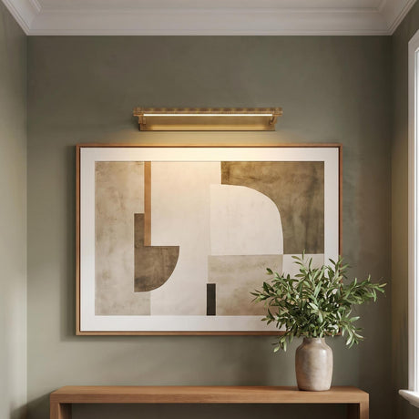 A contemporary entryway featuring the Heath LED Picture Light 24", Aged Brass mounted over abstract artwork above a natural wood console table with a plant.