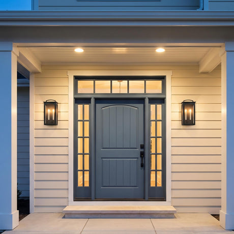 A modern farmhouse entryway featuring two Barlow Outdoor Wall Light, Medium 19", Textured Black fixtures flanking a blue front door with glass sidelights and beige siding.