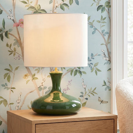 A traditional bedroom featuring the Moselle Table Lamp 21", Glossy Green with a white linen shade on a light wood nightstand against floral chinoiserie wallpaper.