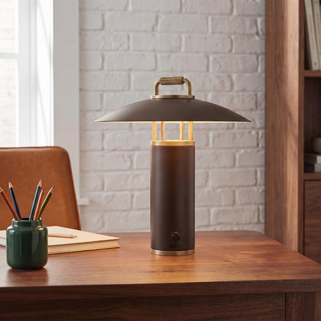 An industrial office with the Bayard Rechargeable Table Lamp 14", Bronze and Patina Brass on a walnut desk beside a white brick wall and leather chair.