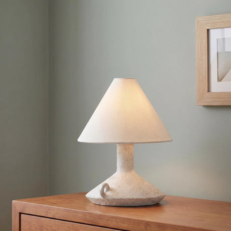 A minimalist bedroom featuring the Gemina Rechargeable Table Lamp 12", Artisan Ceramic White with a linen shade placed on a warm wood dresser against sage green walls.