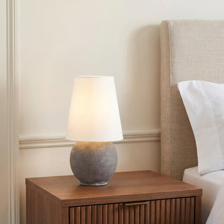 A contemporary bedroom featuring the Inara Rechargeable Table Lamp 15", Artisan Ceramic Gray with a white linen shade on a fluted walnut nightstand beside a beige headboard.