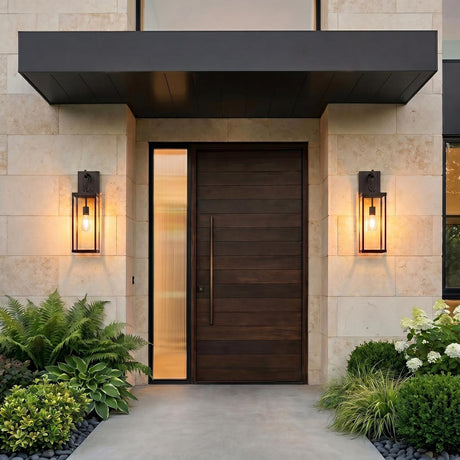 A modern home entry featuring two glowing Lavelle Outdoor Wall Lights in old bronze flanking a dark wood front door on a limestone wall with ferns.