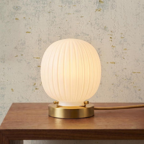 A contemporary living room featuring a Basile Small Table Lamp 8", Brushed Brass and Ribbed Milk Glass resting on a wood console table against a textured wall.
