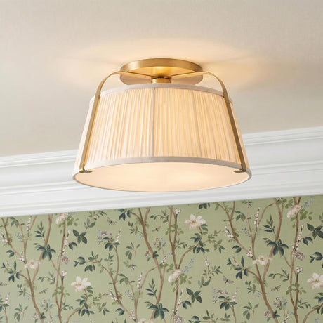 A traditional bedroom with a brushed brass semi-flush mount and pleated linen shade installed on a standard ceiling above sage green floral wallpaper and white molding.