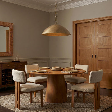 A transitional dining room with a Blaise LED Pendant in feathered brass over a round walnut dining table and four cream boucle chairs on a neutral rug.