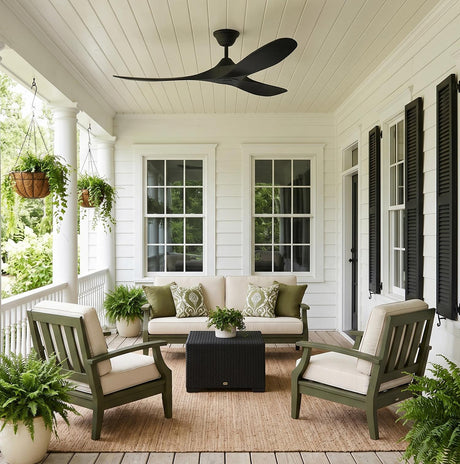 A traditional white siding porch featuring the Egret Outdoor Ceiling Fan 52", Matte Black mounted on a beadboard ceiling above green lounge furniture and black shutters.