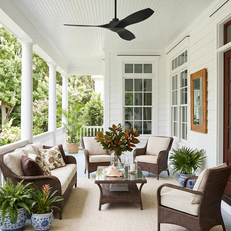 A coastal porch with the Heron Outdoor Smart Ceiling Fan 52", Matte Black on a white beadboard ceiling, featuring white siding and wicker seating with palms.