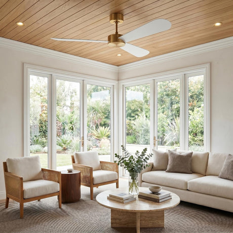 A modern living room featuring the Willet Smart Ceiling Fan 52", Modern Brass and Matte White mounted on a wood ceiling above neutral furniture and large windows.