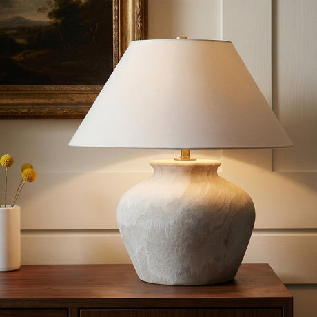 A traditional living room with the Kensington Table Lamp featuring a sand ceramic base and aged brass accents on a dark wood console table against white paneled walls.