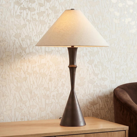 A contemporary living room featuring the Zephyr Table Lamp 28", Bronze with a linen shade on a wood table beside floral wallpaper and a brown armchair.