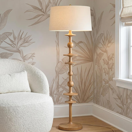 A coastal living room features the Hamish Floor Lamp 63", Natural Oak with a linen shade placed beside a white bouclé chair against botanical leaf wallpaper.