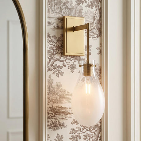 A transitional bathroom with a Geneva Wall Sconce 19", Brass and Ombre Frosted Glass mounted beside an arched brass mirror on brown toile wallpaper.