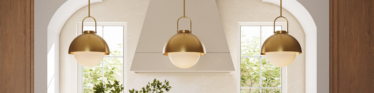 Three Solene pendant lights in aged brass hung in a bright kitchen with oak cabinets.